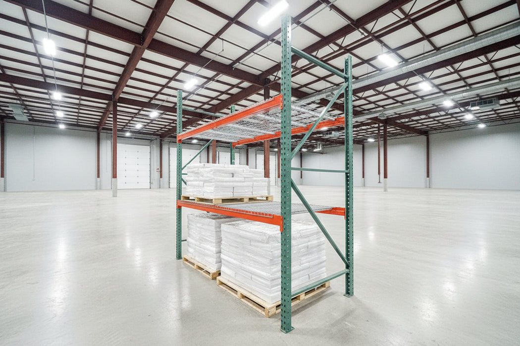 Teardrop pallet rack system with green or blue uprights and orange beams, with a white covering on the rack shelves, situated in an industrial setting.