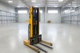 Yellow forklift in a warehouse setting with various equipment and boxes.